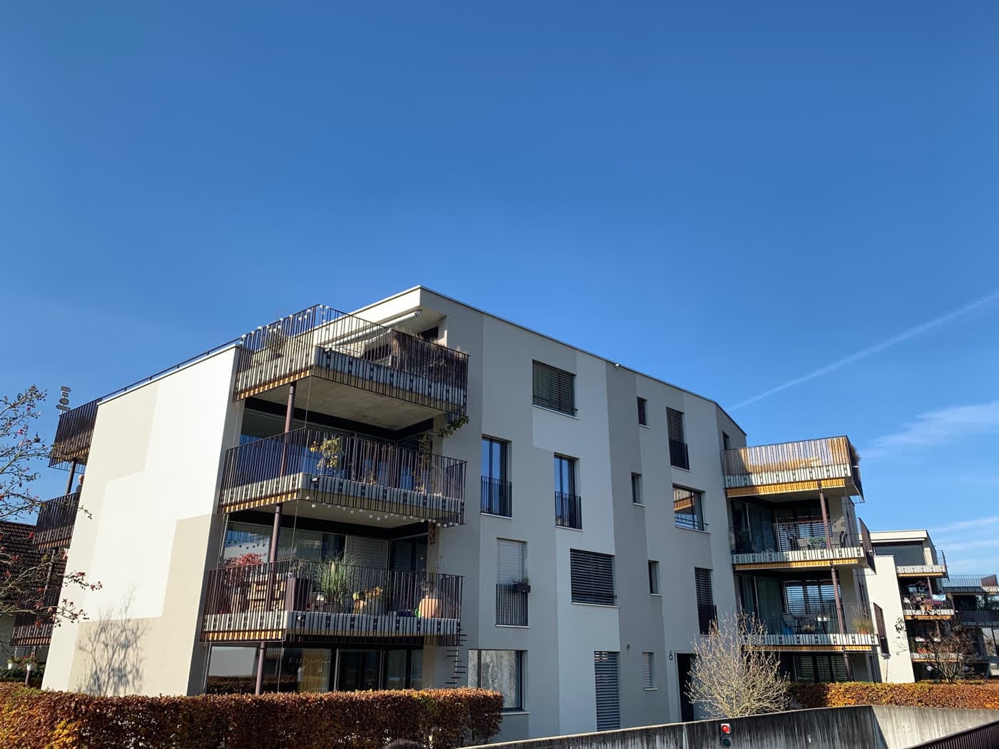 Wohnbau mit Holzbrüstungen an den Balkonen, davor eine geschnittene Hecke