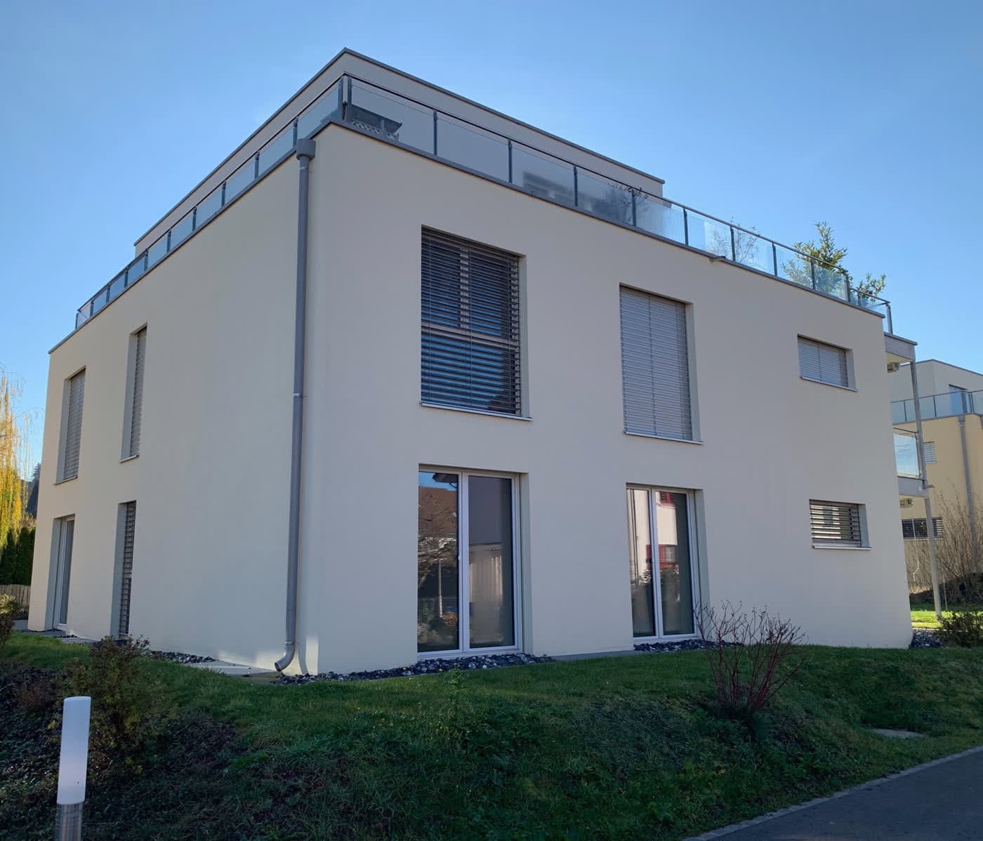 Weisses Mehrfamilienhaus mit Attikageschoss und Rasenböschung