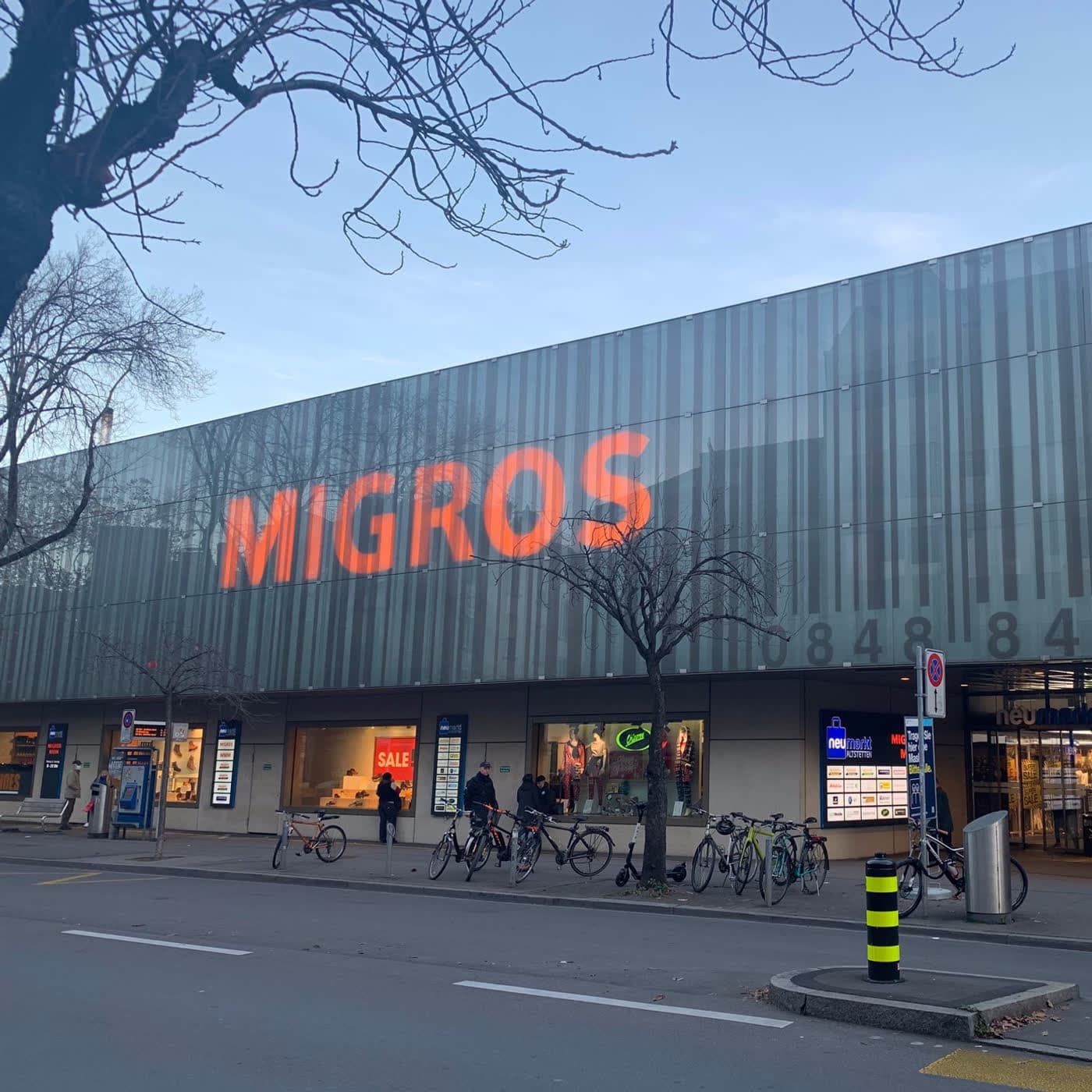 Einkaufszentrum mit gläserner Lamellenfassade, davor Veloparkplätze am Trottoir