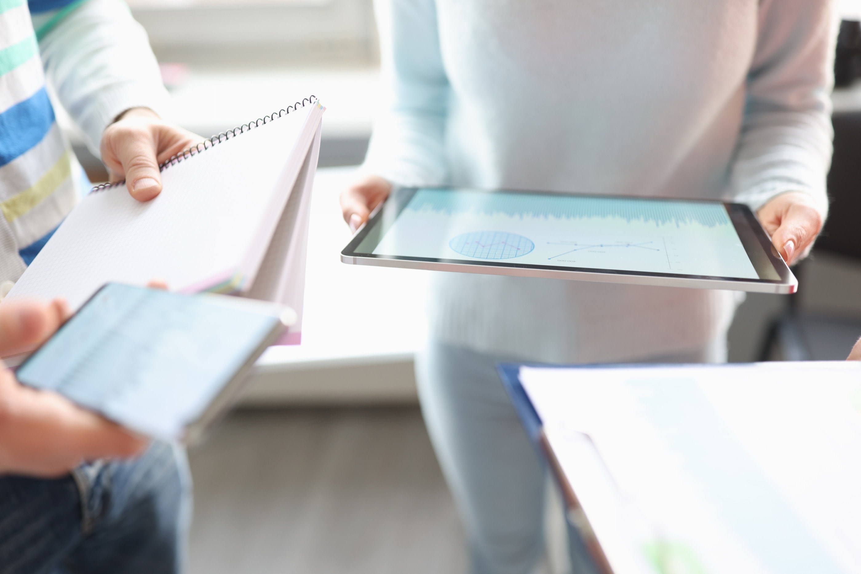 Mitarbeitende halten Tablet, Notizblock und Smartphone in einem hellen Büro und erfassen eine Meldung